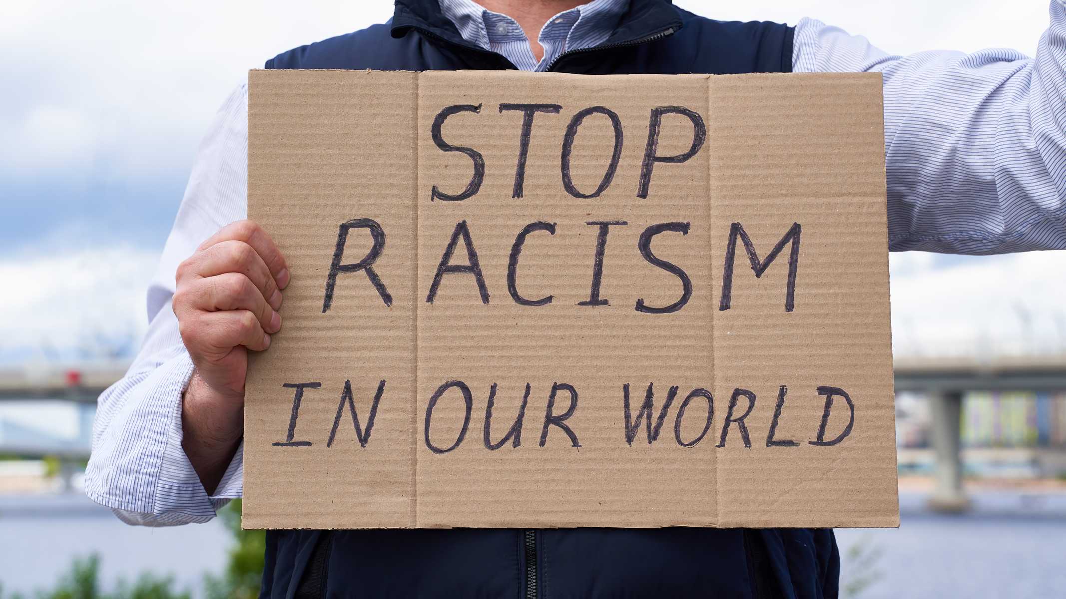 Stop racism concept. Unrecognizable white person holds sign with text against racist.